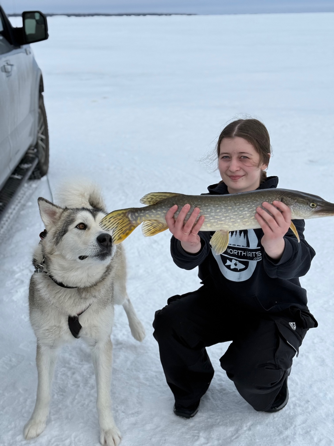 Madison holding a pike while Koda investigates the fish